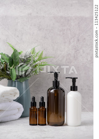 Cosmetic bottles lined up with greenery in a blue vase and a white towel in the background Cosmetic bottles lined up with greenery in a blue vase and a white towel in the background 113425122