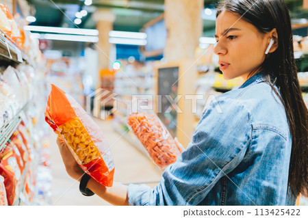 A woman is shopping in a grocery store and is holding a bag of pasta 113425422