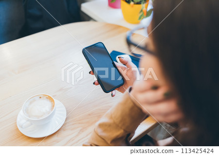 A woman is holding a cell phone in front of a cup of coffee A woman is holding a cell phone in front of a cup of coffee 113425424