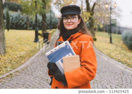A woman wearing an orange coat and hat is holding a stack of books A woman wearing an orange coat and hat is holding a stack of books 113425425