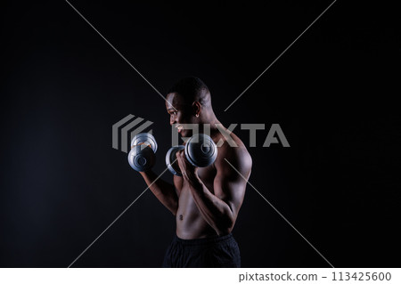 Young man with dumbbells good physique isolated on red and black background. Strength and motivation 113425600