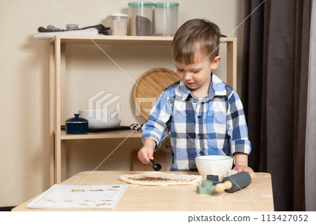 Little child sprinkling dough with flax seeds, making cookies in the kitchen. 113427052
