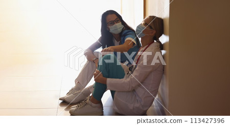 Surgeon in hospital corridor with communicates with doctor sitting on floor 113427396