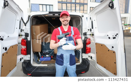Smiling builder holding drill near car. Service repairman concept Smiling builder holding drill near car. Service repairman concept 113427431