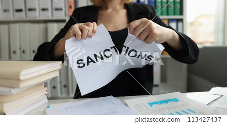 Businesswoman tears up sheet of paper with sanctions inscription 113427437