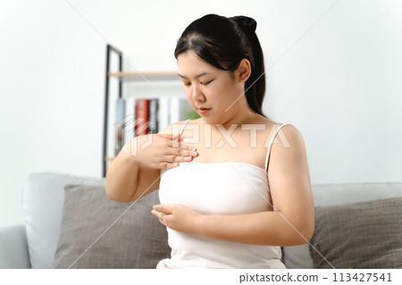 Asian woman checking lumps on her breast for signs of breast cancer by her self at home. 113427541