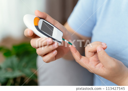 Asian woman using lancet on finger for checking blood sugar level by Glucose meter, diabetes. 113427545