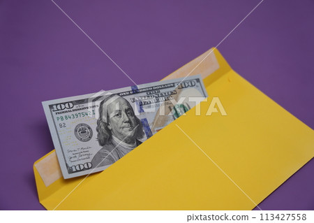 Banknotes in a yellow envelope on a purple background. Bribery concept. Salary in envelopes, fraud. 113427558