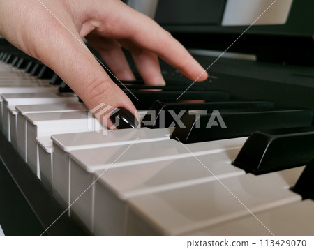 Side view of how the hand of a female musician with painted nails presses the keys of a digital piano, music lessons, playing on the keyboard of a musical instrument 113429070