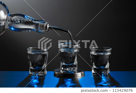 Vodka pouring from the bottle into a glass on a dark background. Vodka pouring from the bottle into a glass on a dark background. 113429076