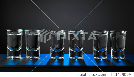 Alcoholic shots of vodka or strong drink in small glasses on a black background. Alcoholic shots of vodka or strong drink in small glasses on a black background. 113429099