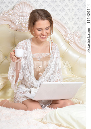 Portrait of young beautiful woman with coffee cup on bed 113429344