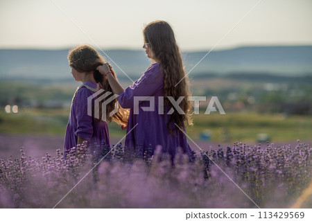 Mom and daughter braiding each other's hair in a field of lavender. The scene is peaceful and serene, with the girls enjoying each other's company and the beauty of their surroundings Mom and daughter braiding each other's hair in a field of lavender. The scene is peaceful and serene, with the girls enjoying each other's company and the beauty of their surroundings 113429569