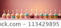 Colorful cupcakes with lit candles are displayed against a pink background, indicating an indoor celebration event marking of joy and celebrating. with free space 113429895