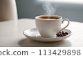 Morning Coffee: A white cup filled with steaming coffee rests on a clean white table, casting a subtle shadow. creating a serene morning scene. 113429898