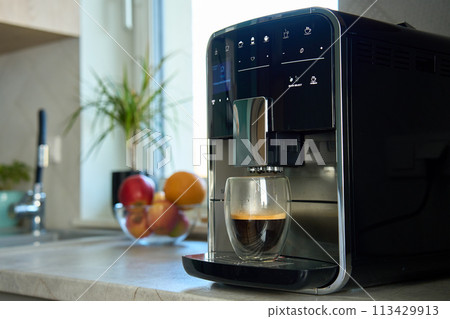 Fresh espresso at morning. Coffee machine in kitchen, close up. Modern coffee maker with freshly brewed coffee in glass cup. Kitchen appliances 113429913