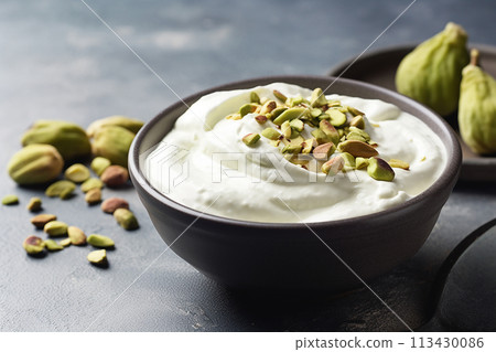 A bowl of creamy yogurt topped with green pistachios alongside fresh green grapes. 113430086