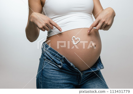 Close up picture of a pregnant womans belly with a cream heart 113431779