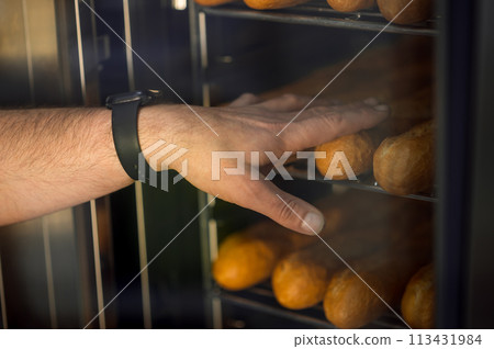 Baker in kitchen near oven with baguettes in bakehouse 113431984