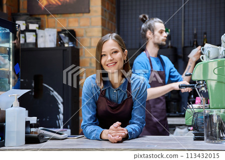 Colleagues partners young man and woman in aprons working together in coffee shop Colleagues partners young man and woman in aprons working together in coffee shop 113432015