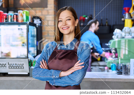 Young woman service worker in apron looking at camera in restaurant, coffee shop 113432064