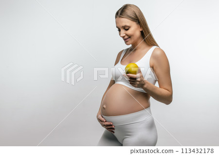 Smiling blonde pregnant woman with apple in hands 113432178