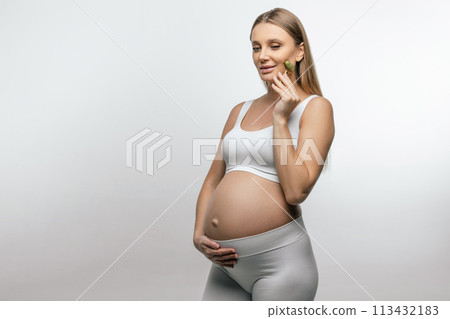 Pretty pregnant young woman with a face roller in hands 113432183