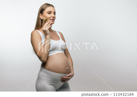 Pretty pregnant young woman with a face roller in hands 113432184