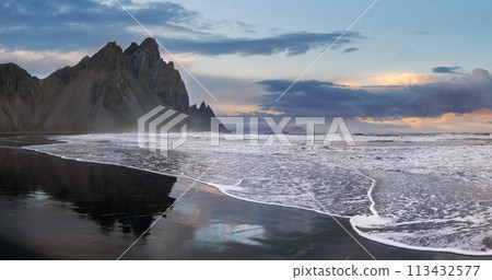 Sunrise Stokksnes cape sea beach and Vestrahorn Mountain with its reflection on wet black volcanic sand surface, Iceland. Amazing nature scenery, popular travel destination. 113432577
