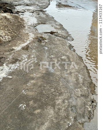 Melting dirty snow on the streets of the city during the daytime in winter. Snow with sand and mud lies on the road. Melting dirty snow on the streets of the city during the daytime in winter. Snow with sand and mud lies on the road. 113433167