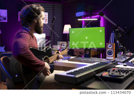 Artist learning to play guitar with internet lessons on greenscreen monitor, watching tutorials for acoustics rehearsal in home studio. Producer learns new string accords for music industry. Artist learning to play guitar with internet lessons on greenscreen monitor, watching tutorials for acoustics rehearsal in home studio. Producer learns new string accords for music industry. 113434070