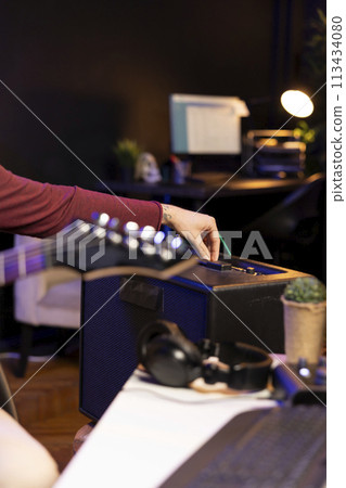 Sound producer adjusting volume levels on home studio amplifier before recording guitar tunes for mixing and mastering session. Male composer creating a new song with stereo gear. Close up. 113434080