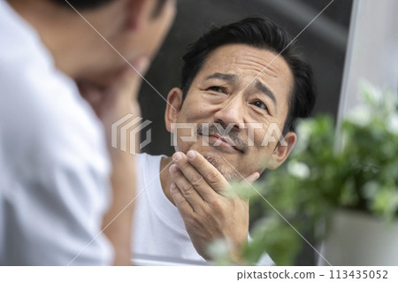 A man in his mid-50s looking in the mirror and putting his hand on his chin Skin care image 113435052