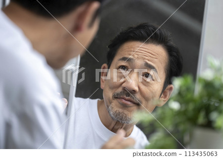 Skin care image of a man in his 50s looking in the mirror Skin care image of a man in his 50s looking in the mirror 113435063