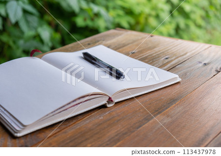 Open white empty paper notepad on wooden table outdoors. Concept of author writing in relaxed cozy atmosphere. Spiritual health digital detox slowing down 113437978