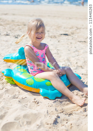 Happy girl sitting and laughing on an inflatable crocodile toy at the beach sunny day 113440263