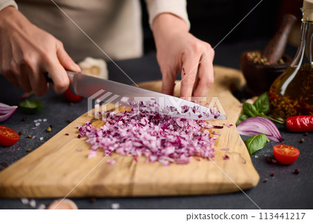 Woman chopping red Mars onion on wooden cutting board at domestic kitchen Woman chopping red Mars onion on wooden cutting board at domestic kitchen 113441217