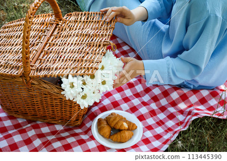A girl on a picnic with a wicker basket and croissants A girl on a picnic with a wicker basket and croissants 113445390