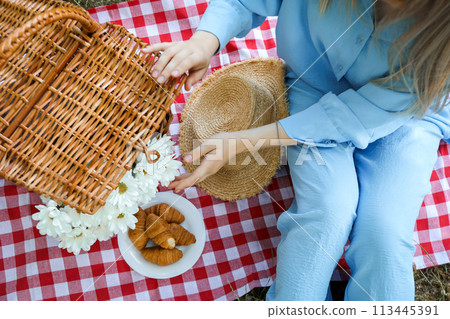 A girl on a picnic with a wicker basket and croissants A girl on a picnic with a wicker basket and croissants 113445391