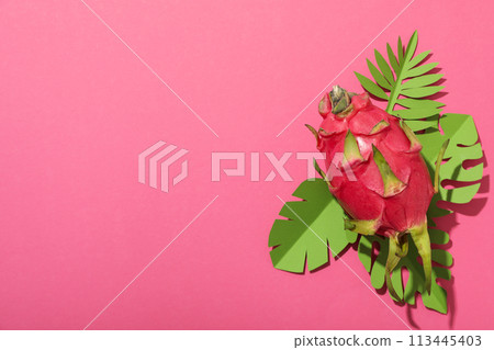 One whole dragon fruit and paper tropical leaves on pink background, space for text One whole dragon fruit and paper tropical leaves on pink background, space for text 113445403
