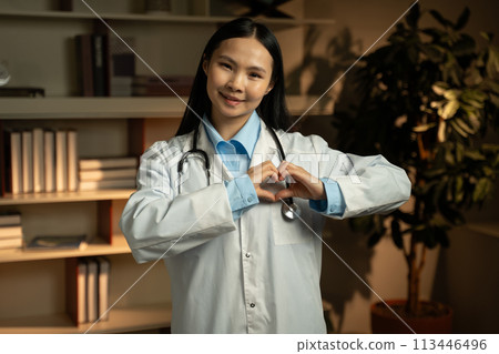 Compassionate Asian Female Doctor Gesturing Heart Sign in Clinic Office 113446496