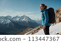 A young happy European woman with a tourist backpack stands on top of a rock in the mountains, travels and enjoys a beautiful view of the mountains, sky or nature. Untouched nature. Tourism and travel 113447367