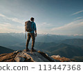 A young happy European man a tourist backpack stands on top of a rock in the mountains, travels and enjoys a beautiful view of the mountains, sky or nature. Untouched nature. Tourism and travel 113447368