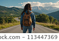 Young positive African American woman with a tourist backpack stands on top of a rock in the mountains, travels and enjoys a beautiful view of the mountains, sky or nature. Untouched nature. Tourism 113447369