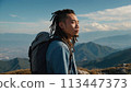 A young happy Chinese man with a tourist backpack stands on top of a rock in the mountains, travels and enjoys a beautiful view of the mountains, sky or nature. Untouched nature. Tourism and travel 113447373