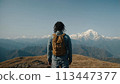 A young happy Chinese man with a tourist backpack stands on top of a rock in the mountains, travels and enjoys a beautiful view of the mountains, sky or nature. Untouched nature. Tourism and travel 113447377