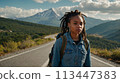 Young positive African American woman with a tourist backpack stands on top of a rock in the mountains, travels and enjoys a beautiful view of the mountains, sky or nature. Untouched nature. Tourism 113447383