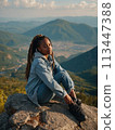Young positive African American woman with a tourist backpack stands on top of a rock in the mountains, travels and enjoys a beautiful view of the mountains, sky or nature. Untouched nature. Tourism 113447388