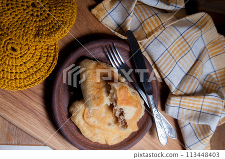 Clay plate of fried meat pies with cutlery on wooden table. 113448403