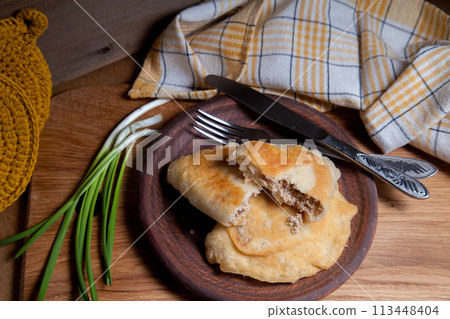 Clay plate of fried meat pies with cutlery and green onion on wooden table. 113448404